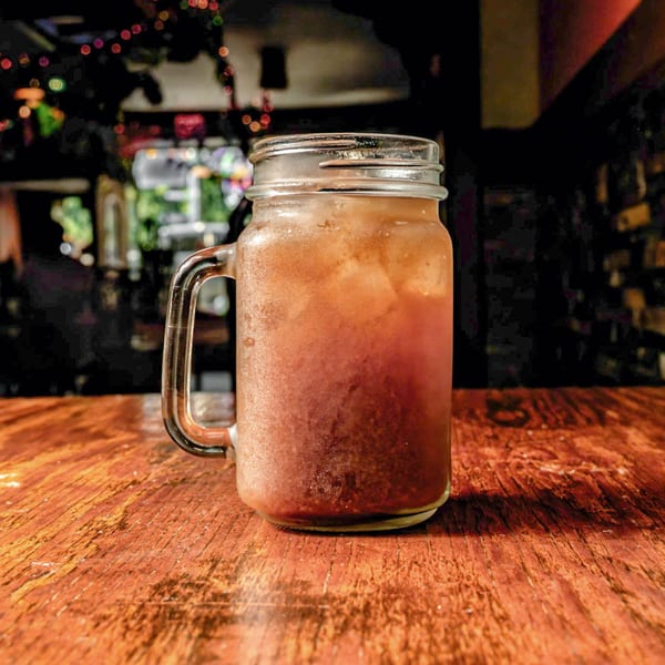 A frosty mason jar filled with a reddish-brown iced drink sits on a wooden table.