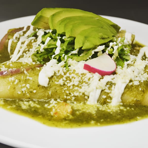 Avocados Mexican Grill's enchiladas verdes, topped with avocado slices, lettuce, cheese, and a radish.