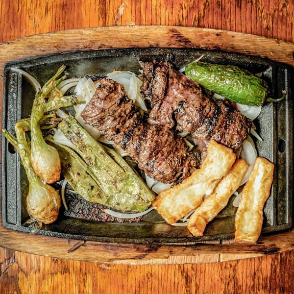 Sizzling Mexican fajitas with grilled steak, onions, peppers, and fried cheese on a cast iron skillet.