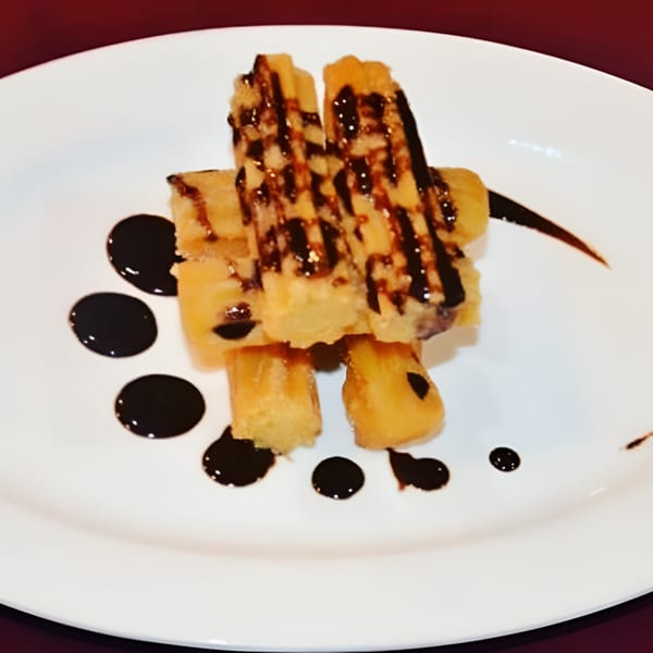 Golden churros drizzled with dark chocolate sauce, artfully arranged on a white plate.