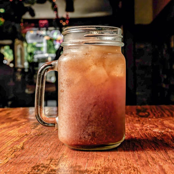 A frosty mason jar filled with a red beverage and ice sits on a rustic wooden table.