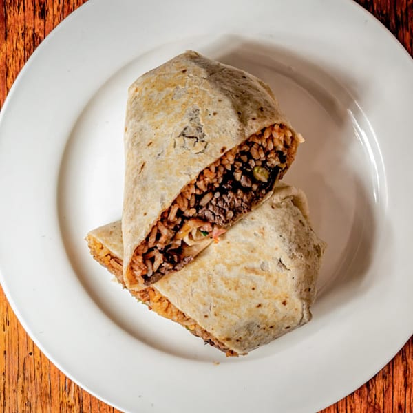 A large, cut burrito from Avocados Mexican Grill, filled with rice and meat, on a white plate.