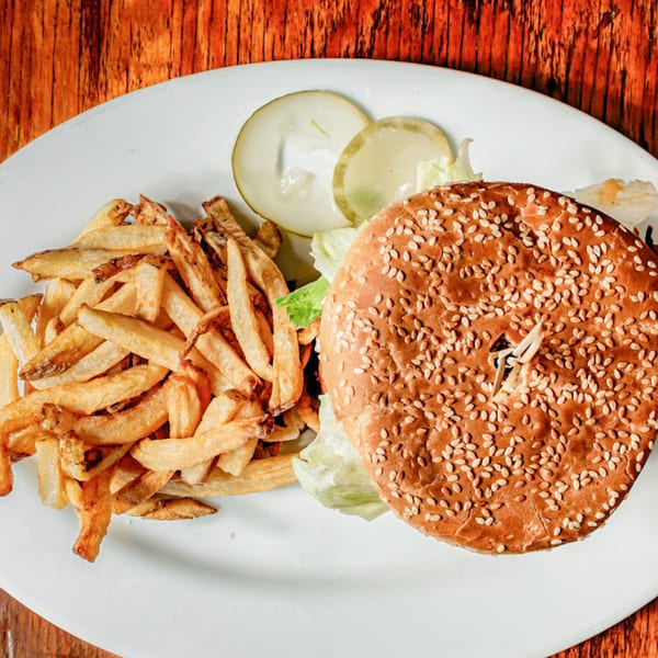 A burger with sesame seed bun, lettuce, and pickles, served with a side of fries.